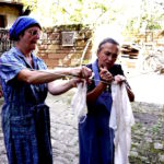 Zwei Frauen in Schürze und mit Kopftuch hängen Wäsche auf ein Wäschezeil